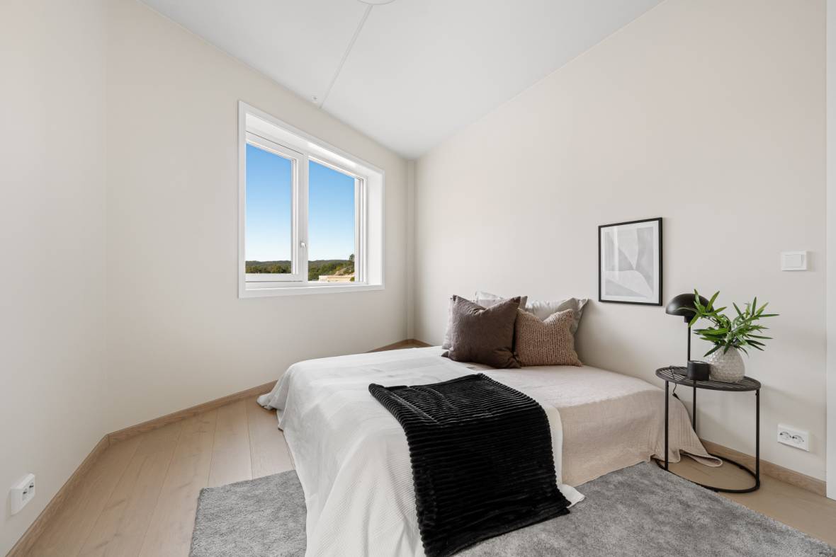 Stylet soverom i nybygg med dobbeltseng, tekstiler og kunst